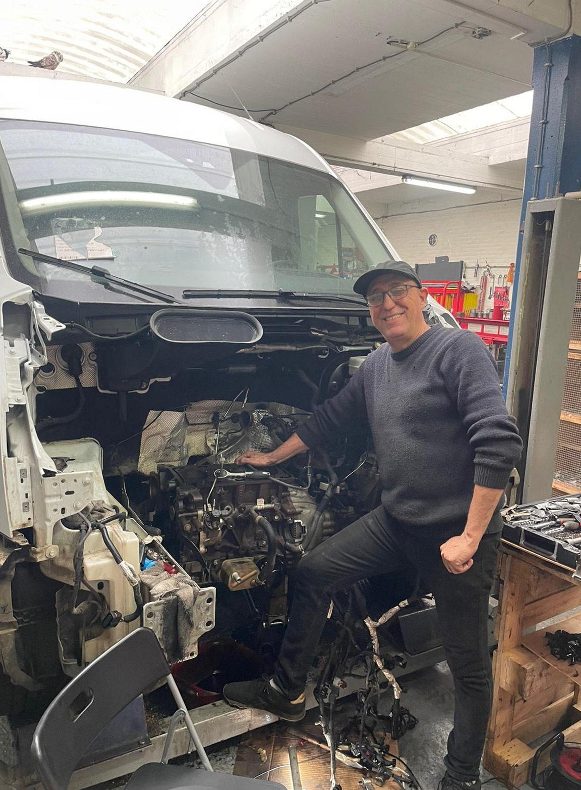 Een man in de werkplaats bij een bestelbus met de motor eruit
