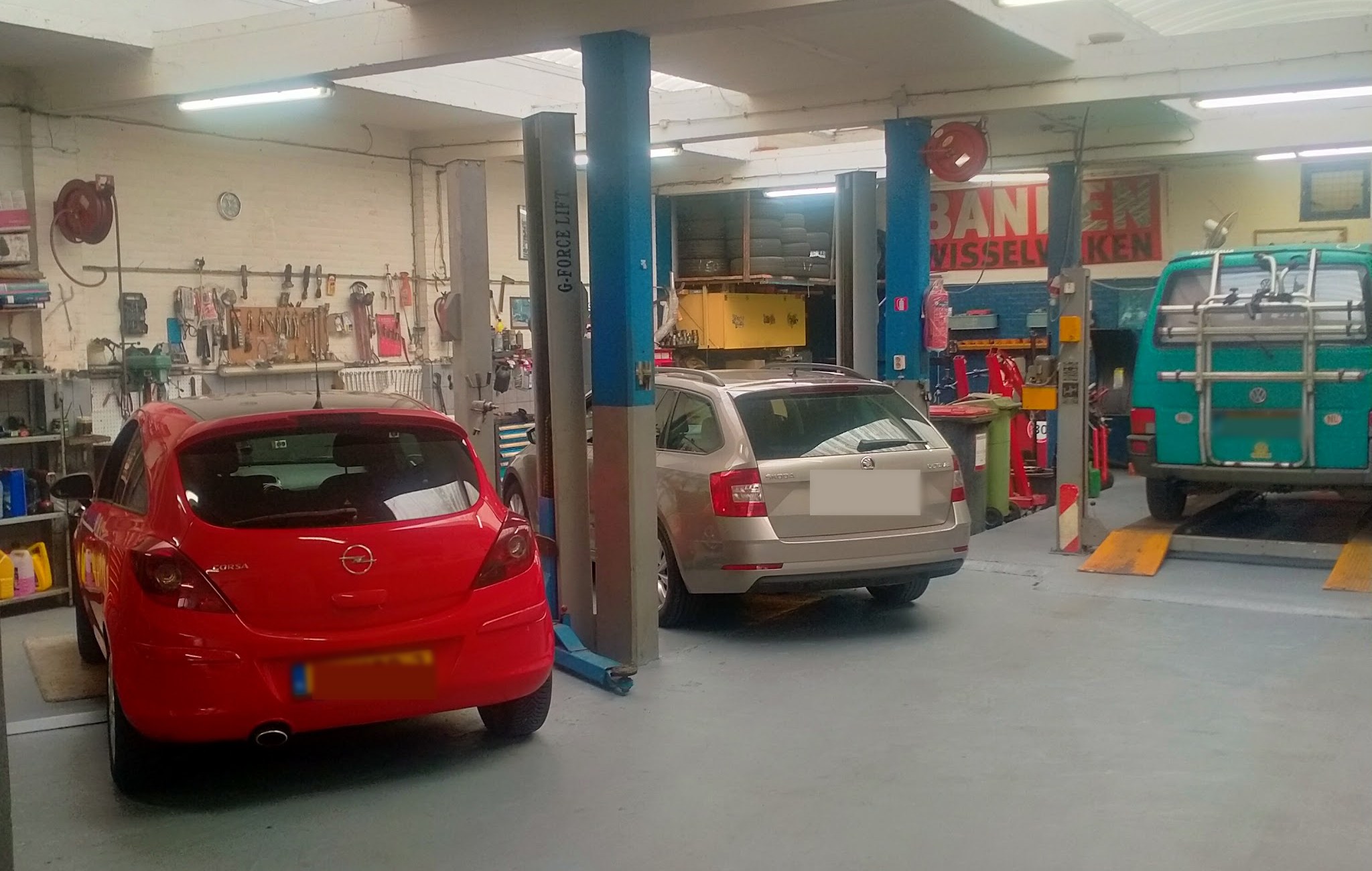 De werkplaats van Sairan Auto Service: twee hefbruggen, een rode Opel Corsa, een stationwagen en een VW-bus