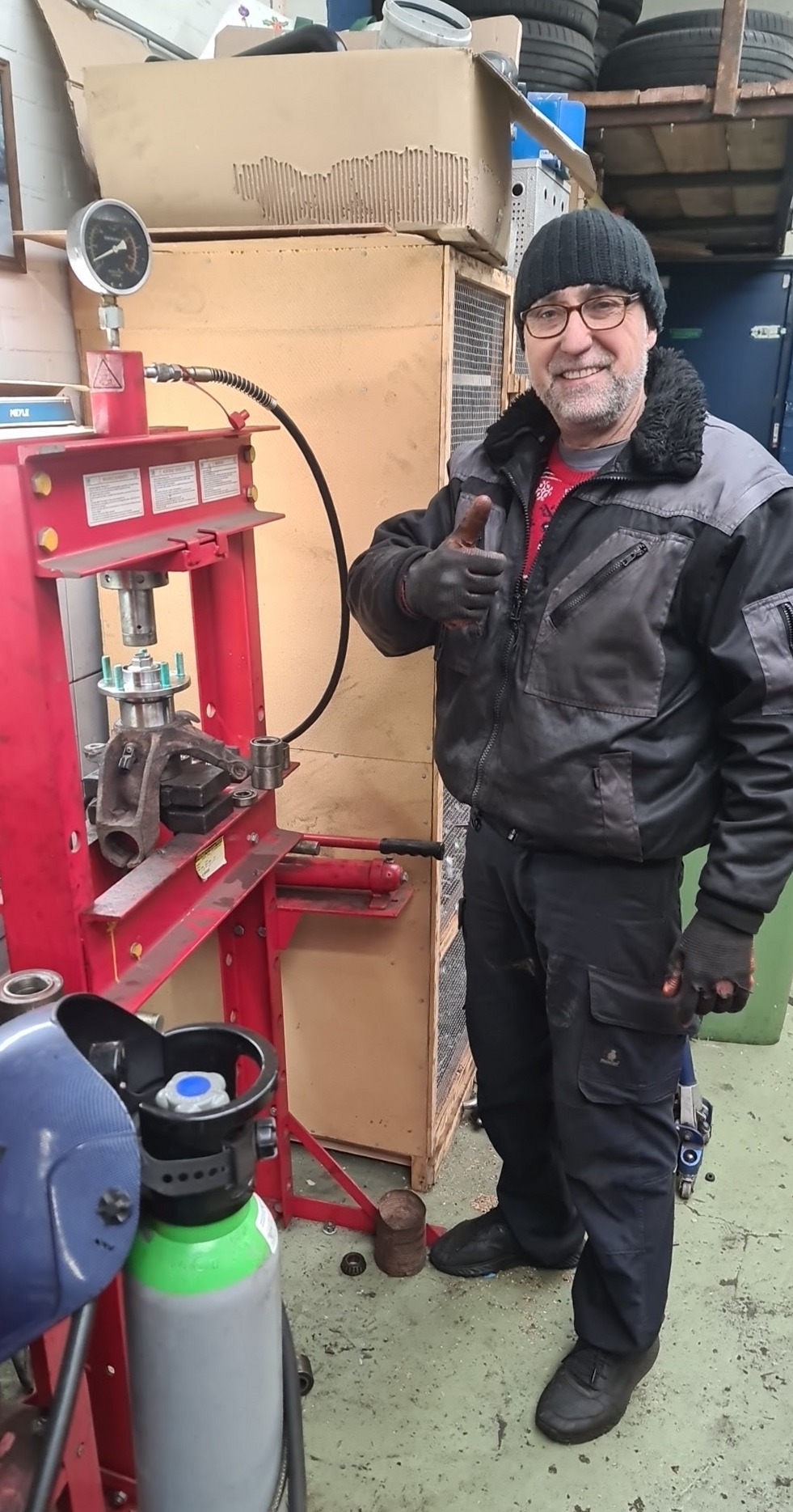 Een man steekt zijn duim op naast een hydraulische pers in de werkplaats